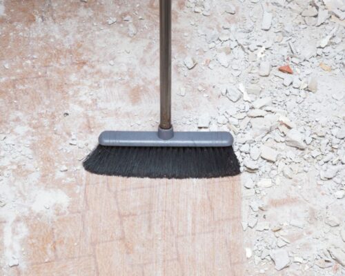 Broom sweeping concrete pieces from floor. Cleaning garbage after repair work of home. Closeup.