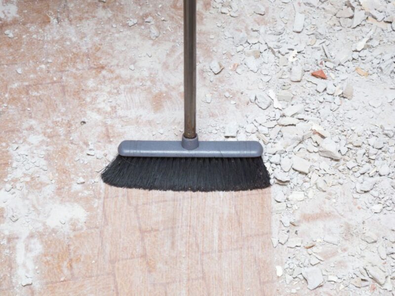 Broom sweeping concrete pieces from floor. Cleaning garbage after repair work of home. Closeup.